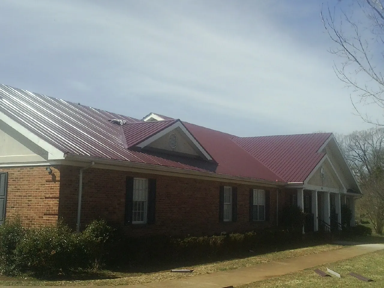 Red metal roof with gabled entries on a long brick building, from a Hail Damage Roof Repair job in Sherwood